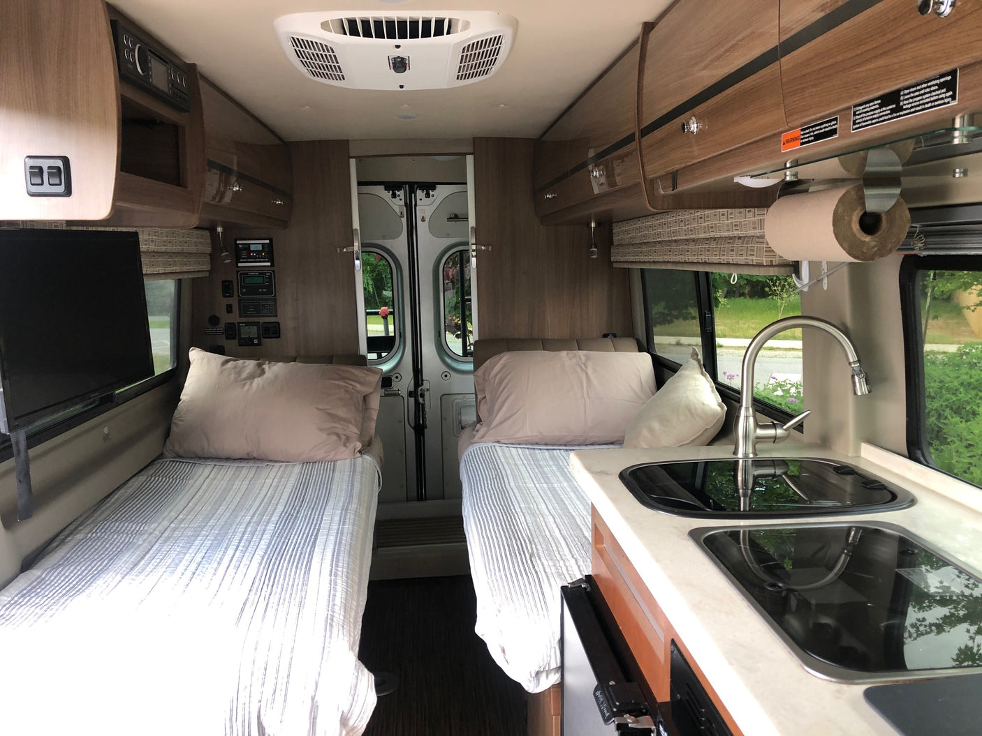 RV rental interior featuring twin beds, a compact kitchen with sink/stovetop, and ample overhead storage.