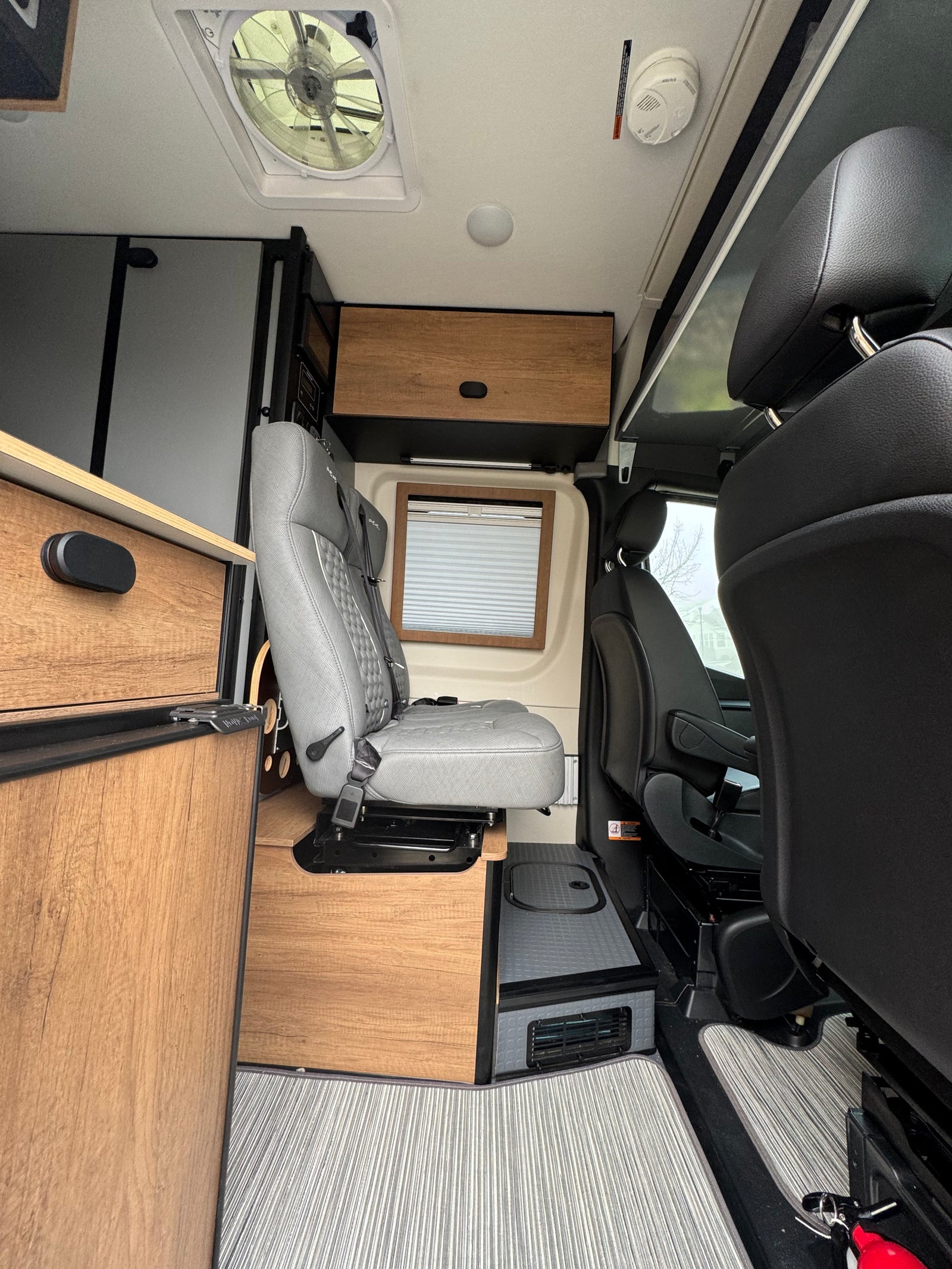 RV rental interior with a gray swivel seat, wooden storage, ceiling fan, and textured flooring, ready for travel.