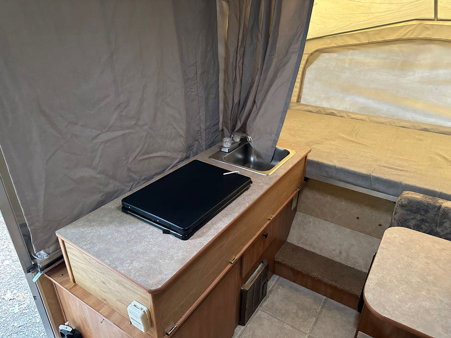a pop-up camper's comfortable bed with light-colored mattress and canvas tent walls.|RV rental interior: cozy pop-up camper with kitchen