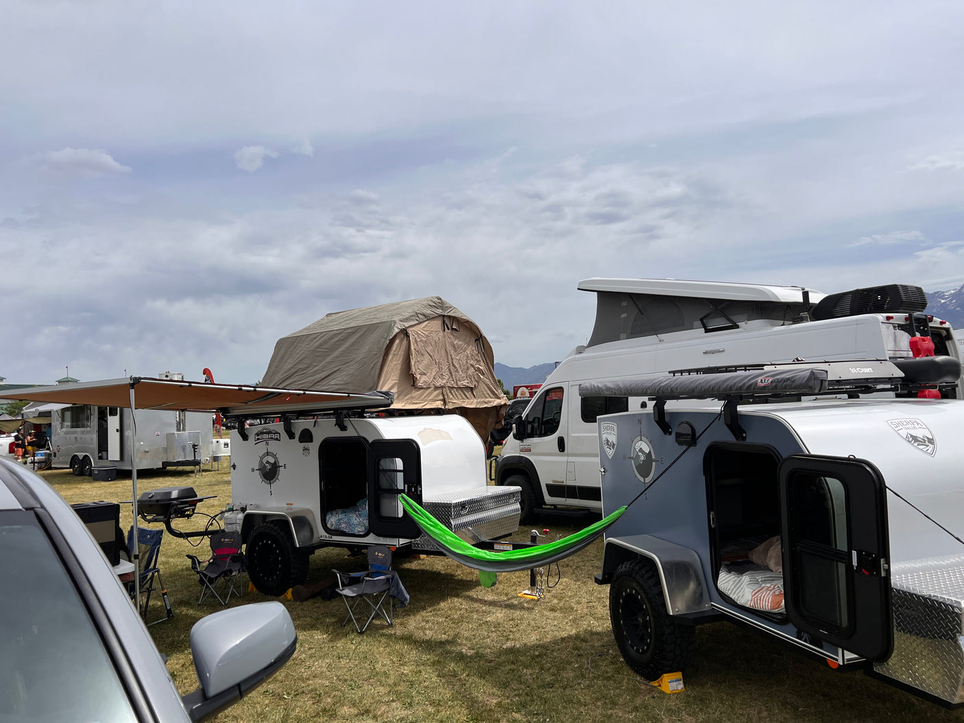Explore diverse RV rental options! This vibrant camping scene features teardrop trailers, a rooftop tent, and a camper van with a hammock.