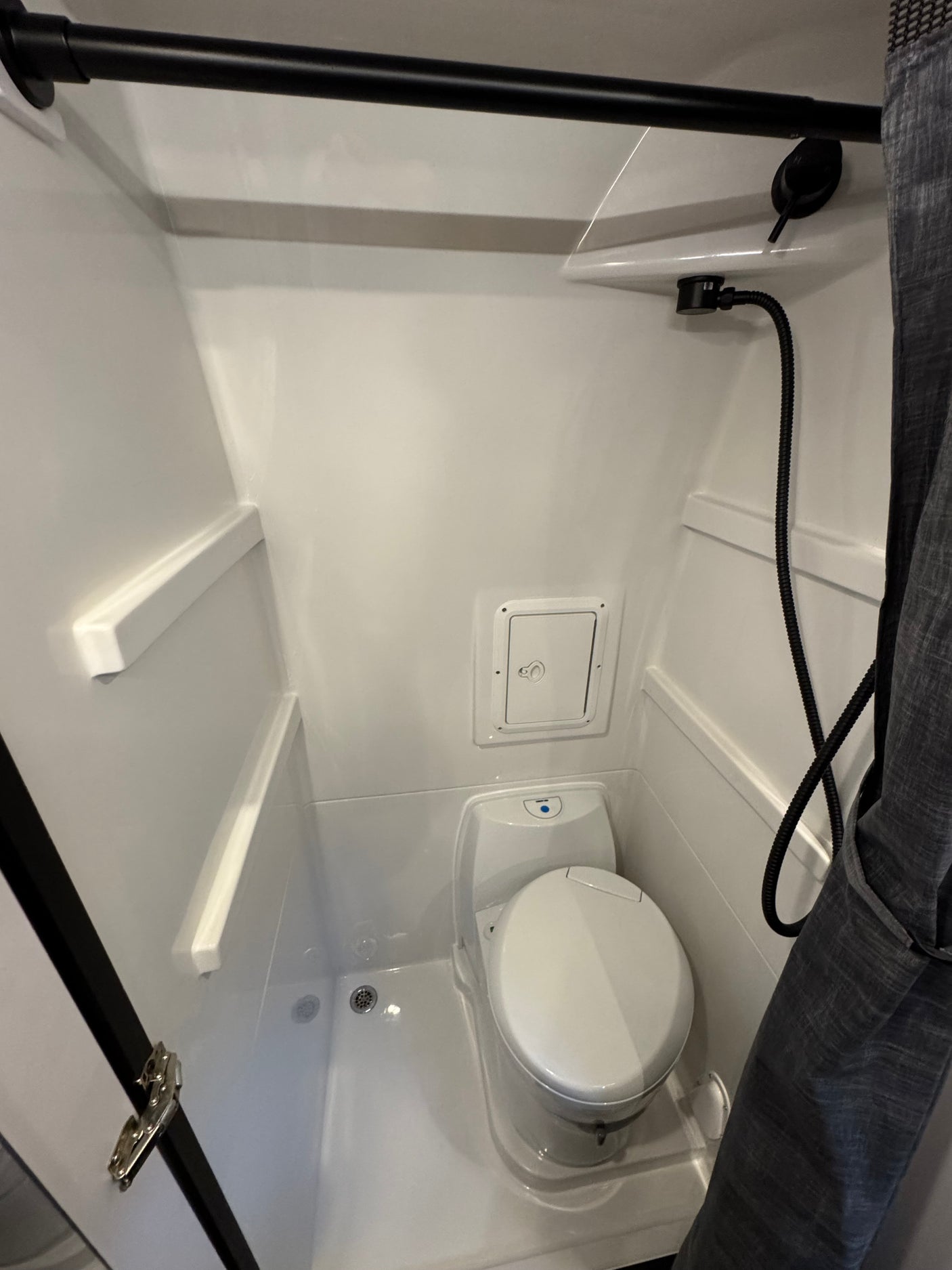 Inside an RV rental: a clean, compact wet bath featuring a toilet, handheld shower, and integrated shelves.