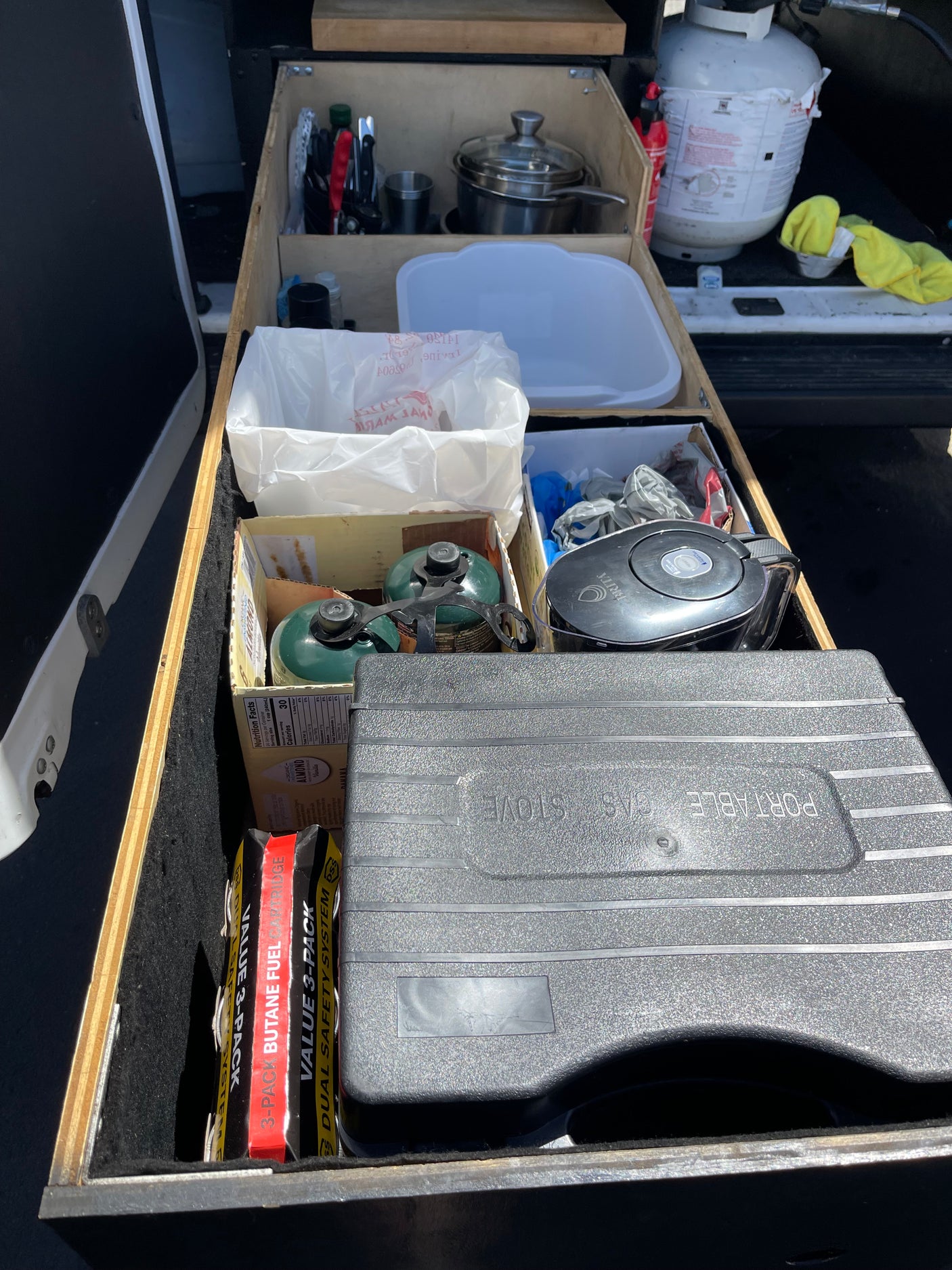 RV rental storage: Organized camping kitchen gear including portable gas stove, fuel, pots, Brita filter, and propane tank.
