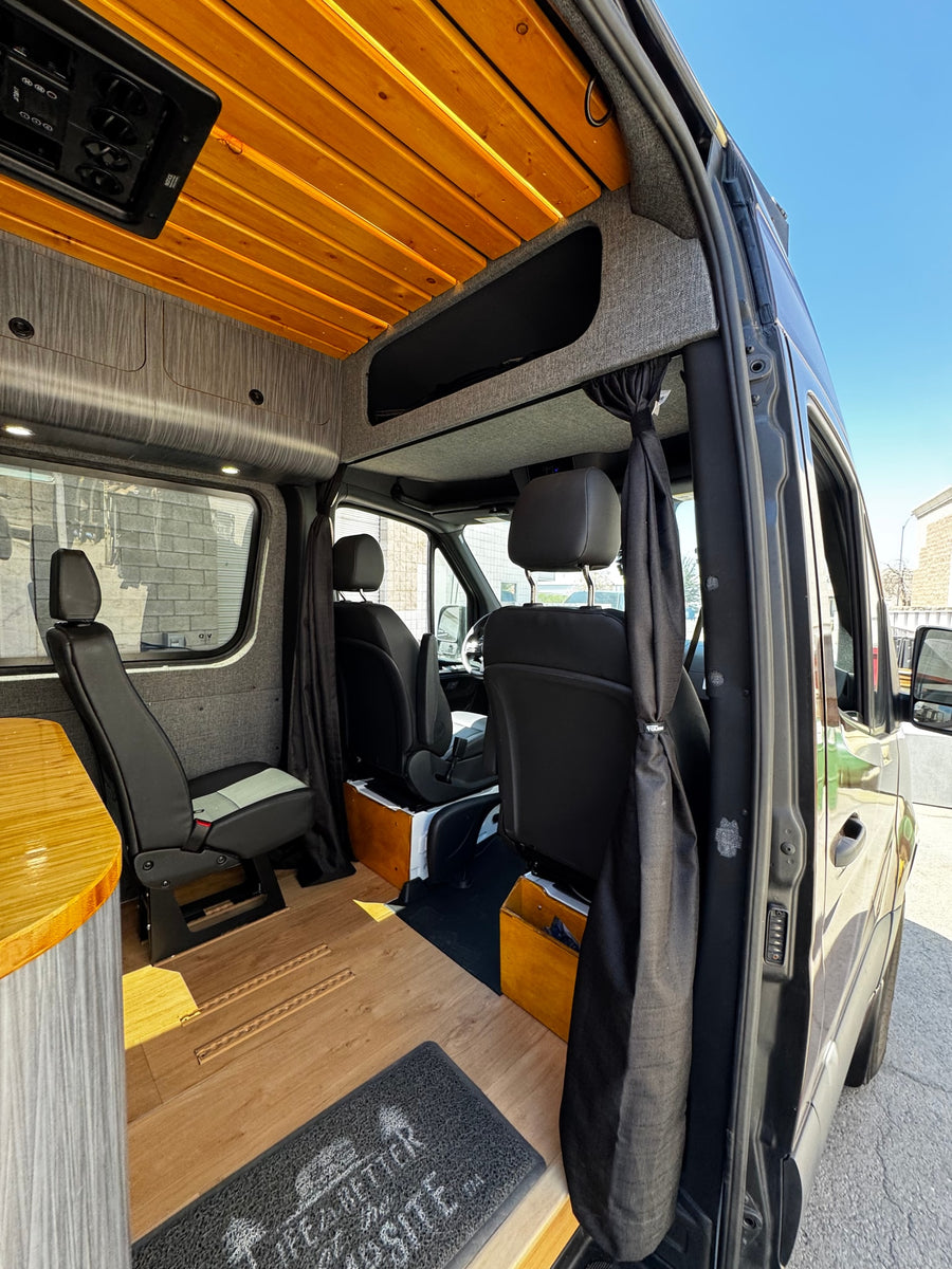 Interior of a custom RV rental camper van featuring a warm wood ceiling, modern grey walls, flexible seating, and hardwood floors.