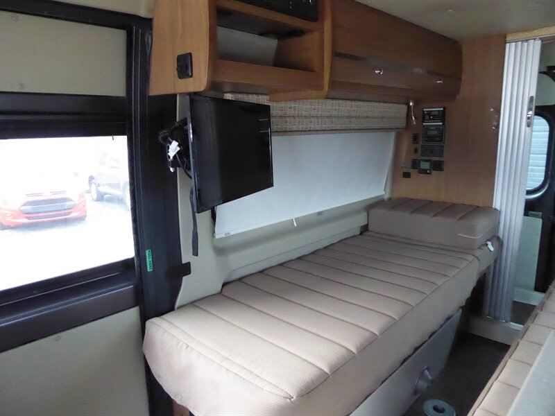 with a compact kitchen on the left & a mounted TV on the right.|Inside an RV rental van: rear view shows compact shower
