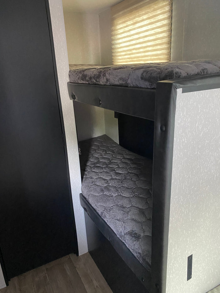Explore this RV rental's comfy bunk beds! A practical interior sleeping area with grey mattresses & window blinds.