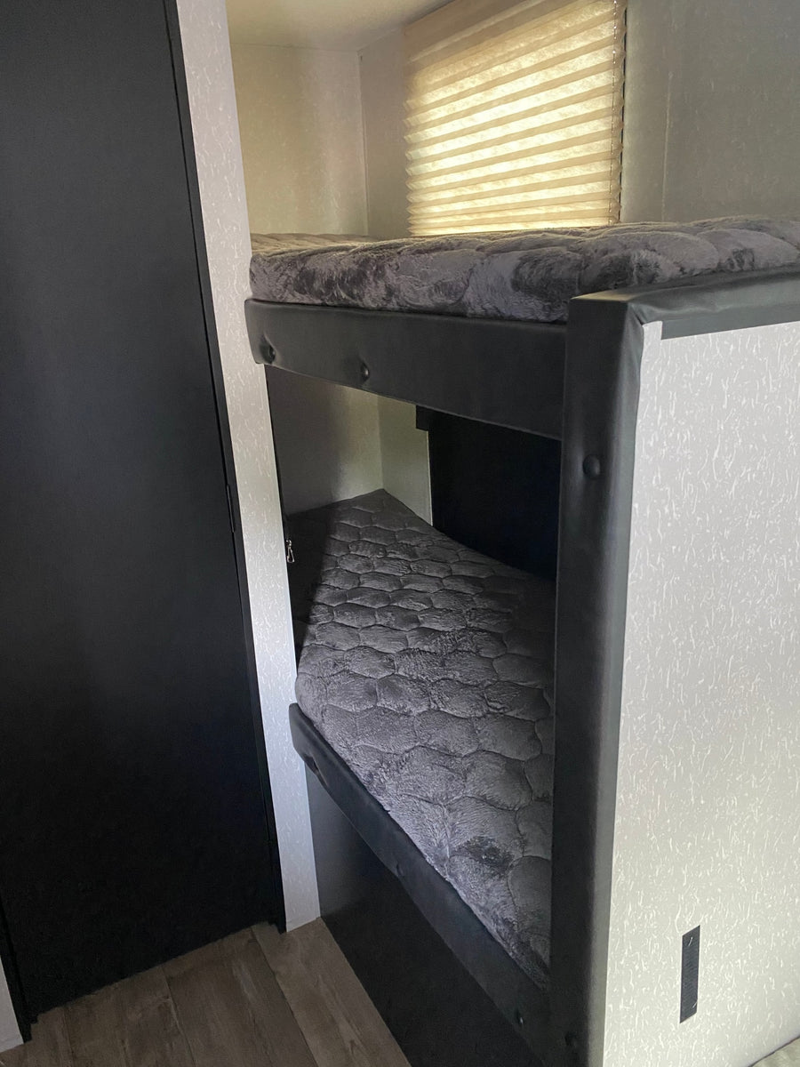 Explore this RV rental's comfy bunk beds! A practical interior sleeping area with grey mattresses & window blinds.