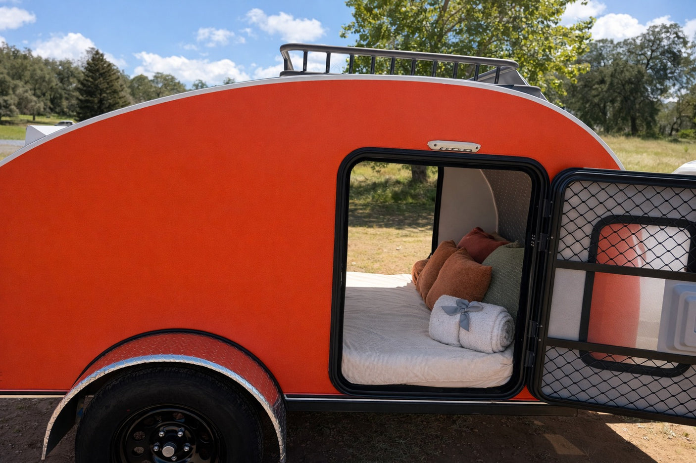 Vibrant orange teardrop RV rental, door open to reveal a comfortable bed. Ready for your next camping trip.