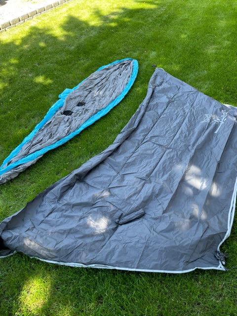 Outdoor RV rental setup: a grey tent footprint/rainfly and blue hammock laid on green grass.