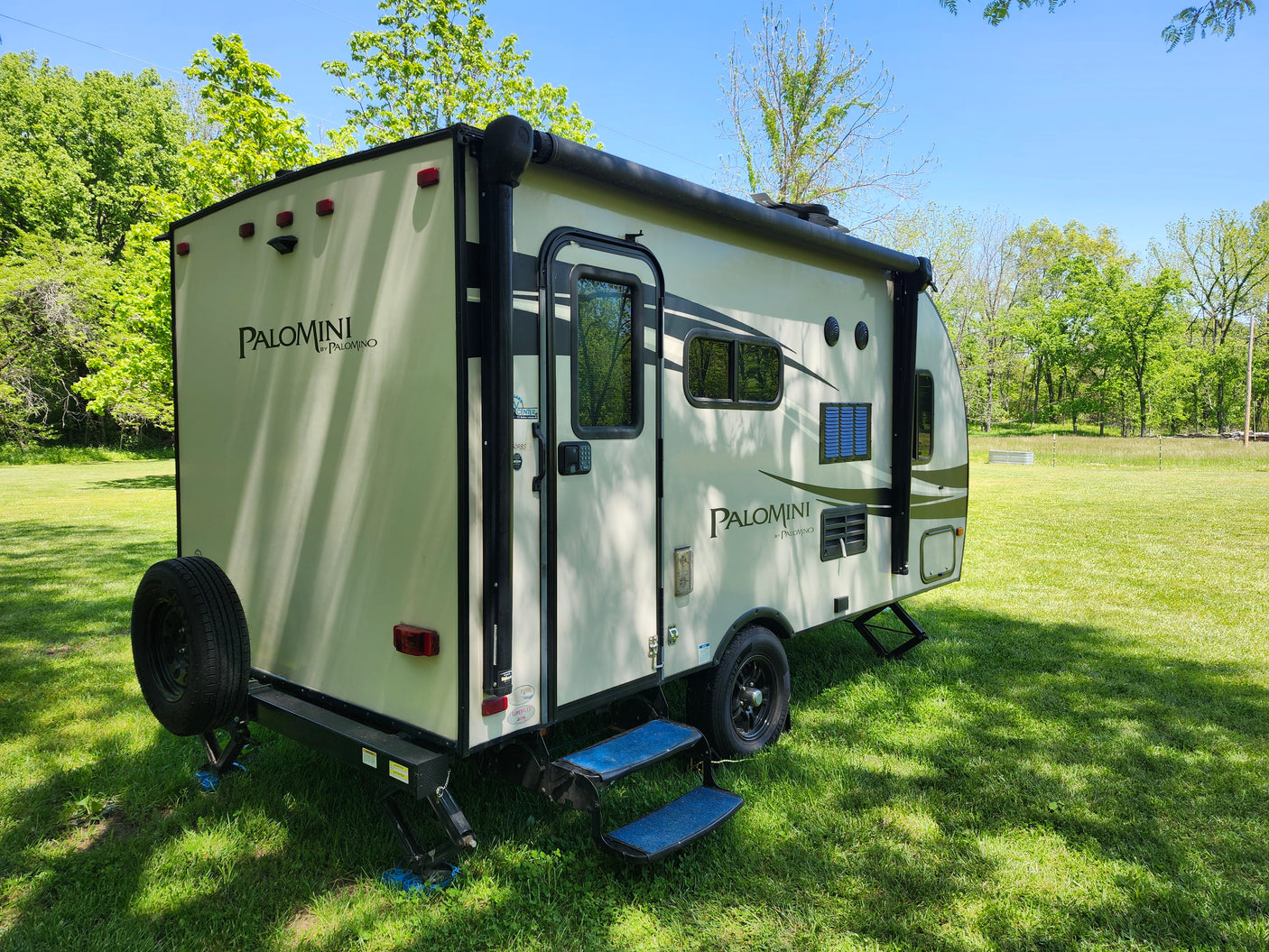 Discover this Palomini travel trailer, an ideal RV rental. Parked in a sunny green field, ready for outdoor camping adventures.