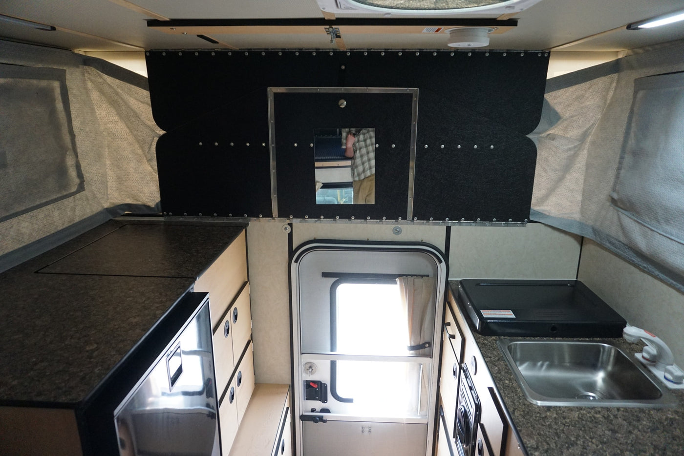 Explore this RV rental's interior: a compact pop-up camper kitchen with sink, stovetop, fridge, and storage. — photo 7