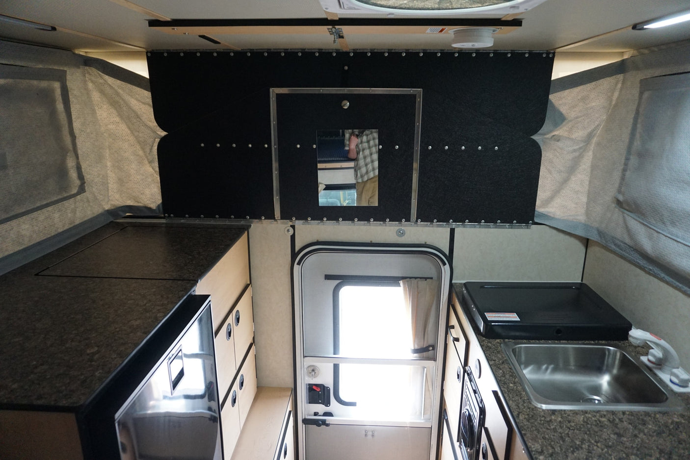 Explore this RV rental's interior: a compact pop-up camper kitchen with sink, stovetop, fridge, and storage.