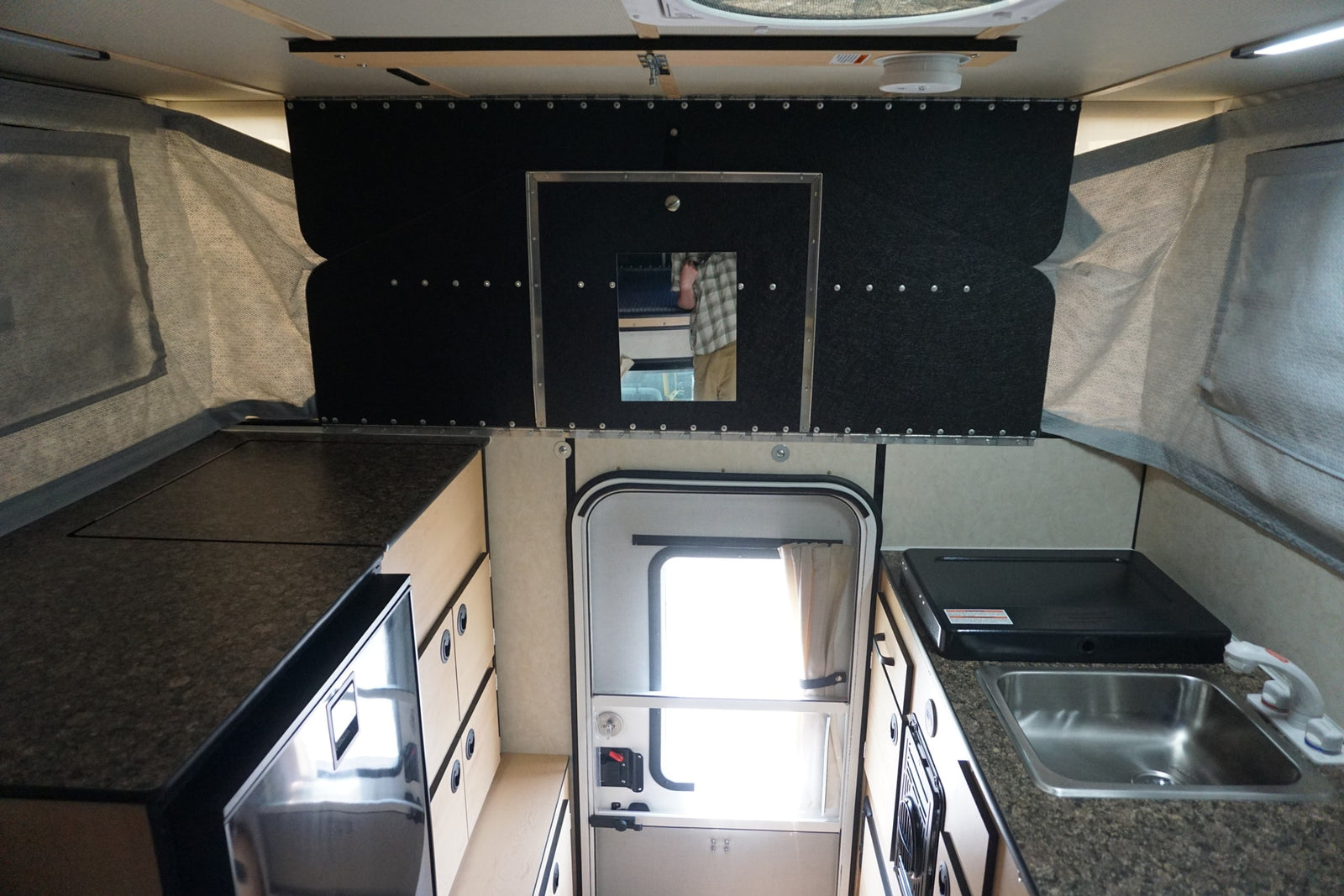 Explore this RV rental's interior: a compact pop-up camper kitchen with sink, stovetop, fridge, and storage.