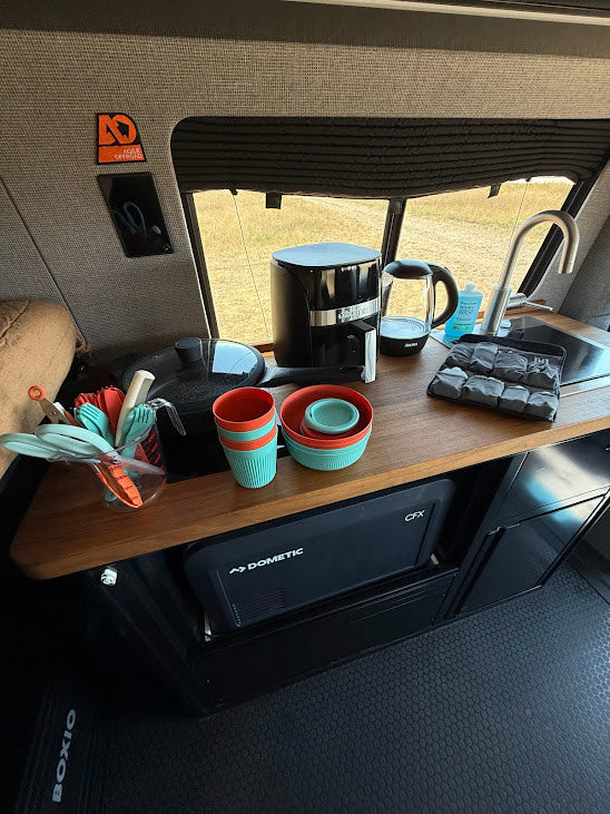 Compact RV rental kitchen featuring Dometic fridge, coffee maker, and organized cooking essentials for road trips.