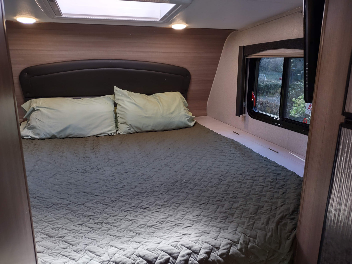 Spacious RV rental bedroom with a comfy bed, skylight, and window view. Includes soft pillows & quilted comforter for relaxing travel.