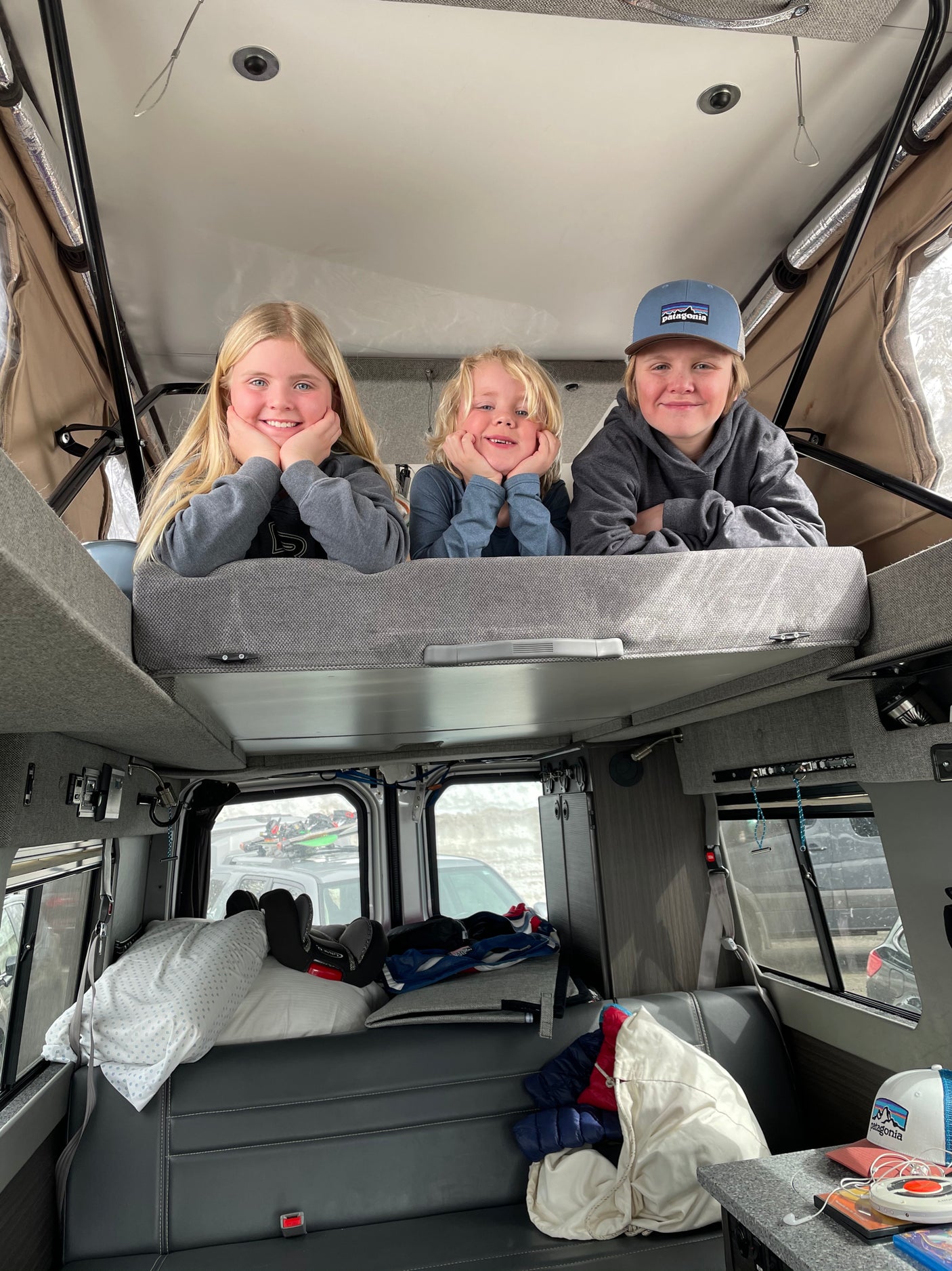 Cozy RV rental interior with three happy kids on the top bunk, enjoying their travel adventure.