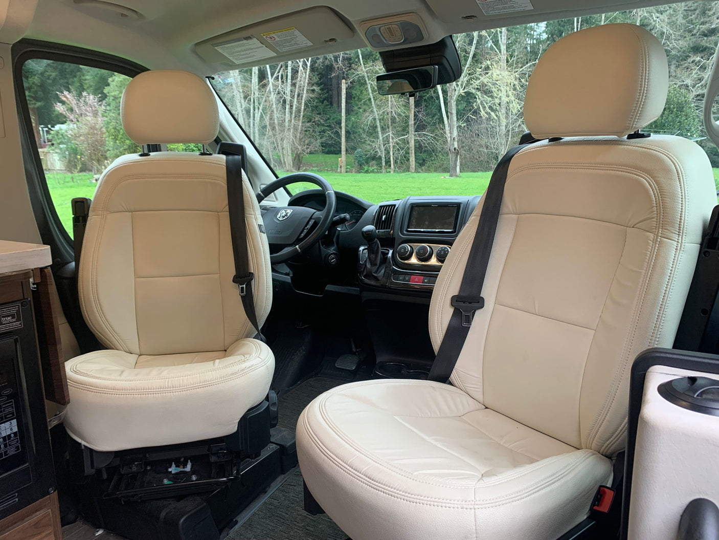 Spacious rv rental interior featuring cream swivel seats, driver's cockpit, and scenic views. Ideal for comfortable travel.