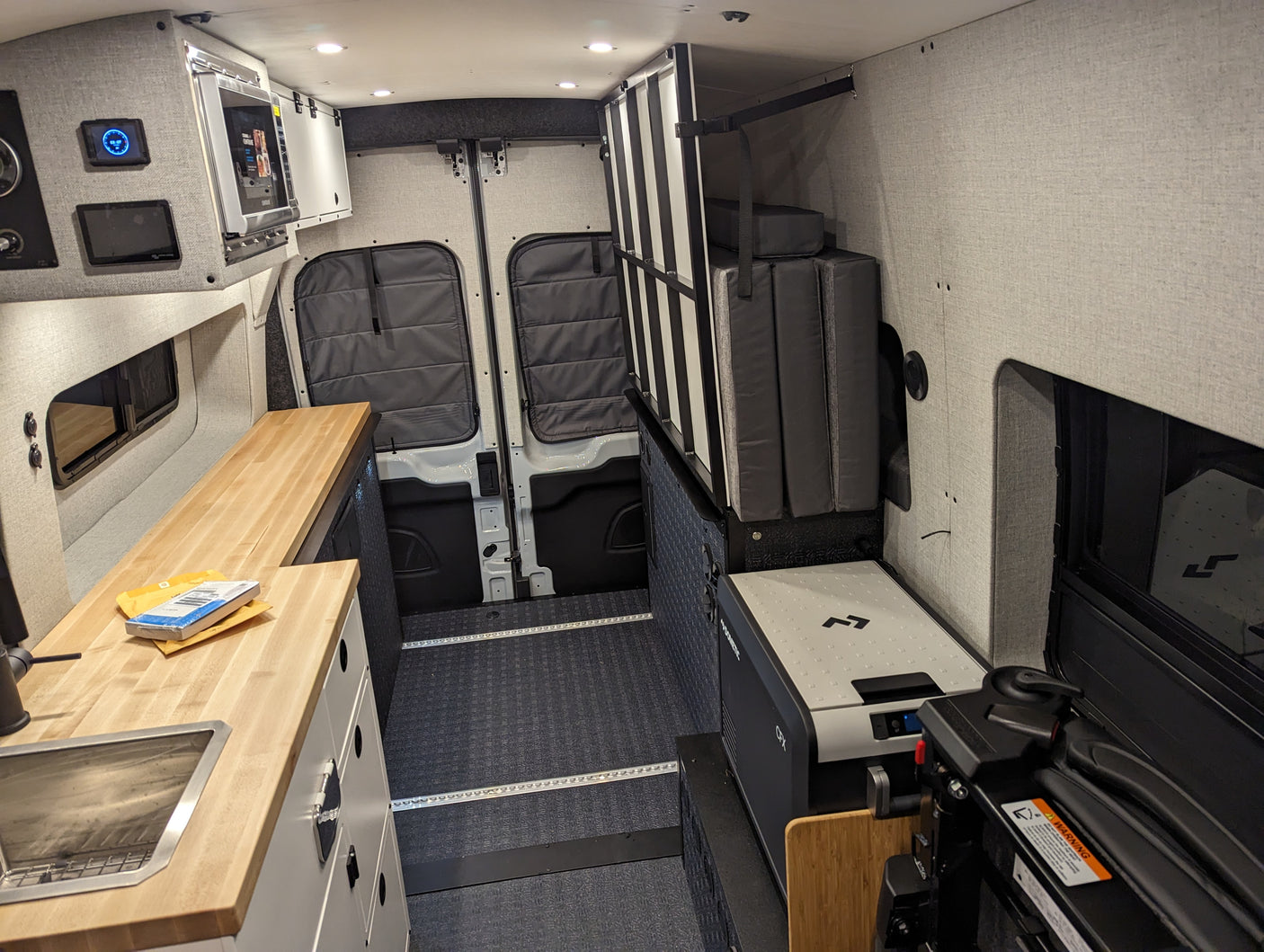 Spacious rv rental interior featuring a compact kitchenette with sink, microwave, foldable bed, and Dometic fridge.