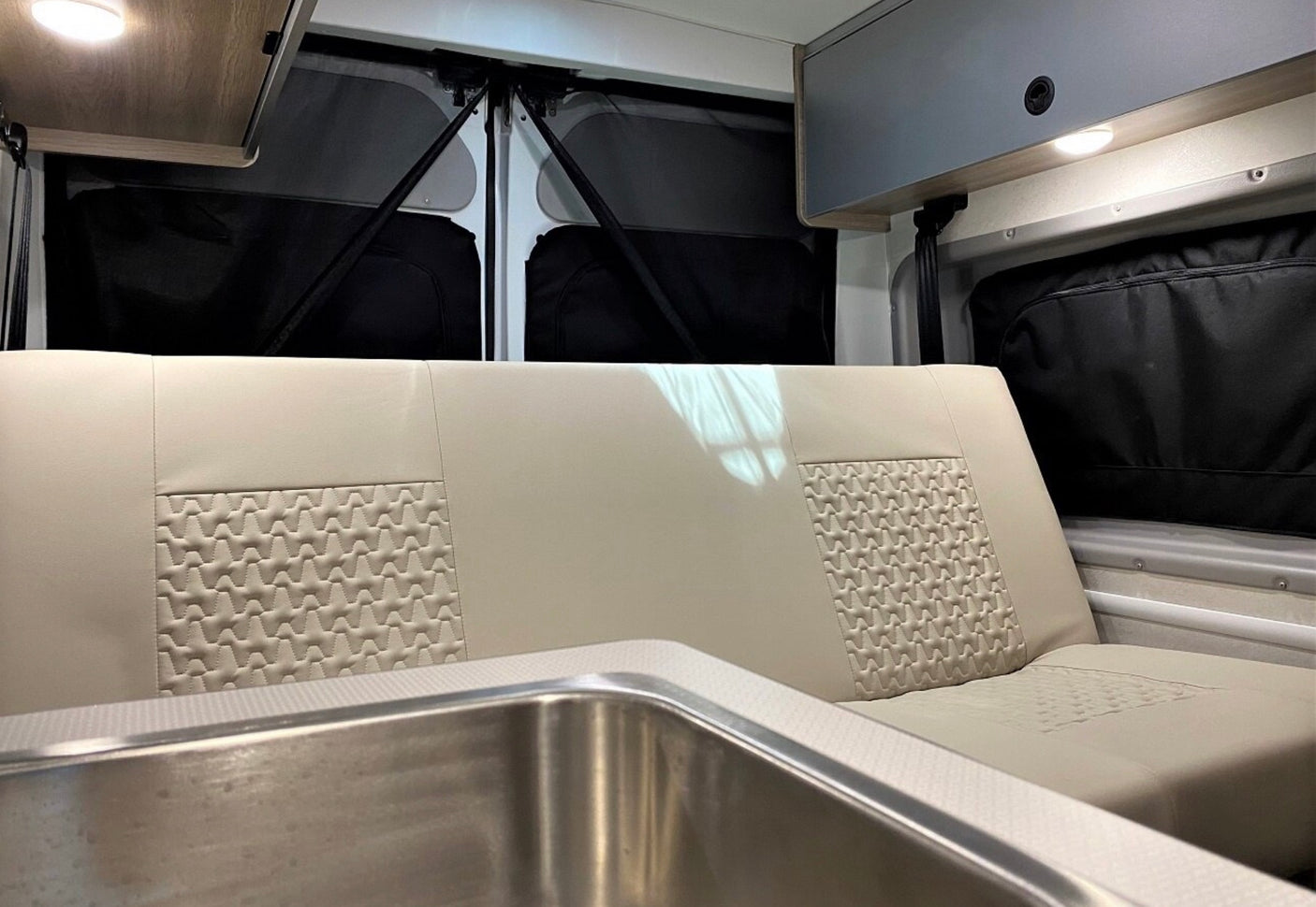 RV rental interior: light-colored bench with quilted design, stainless sink, and overhead storage for comfortable travel.
