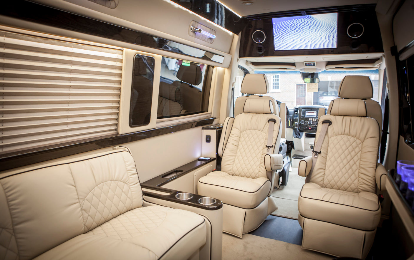 Experience luxury with this spacious van interior, ideal for an RV rental, featuring plush cream seating, a large screen, and elegant lighting.