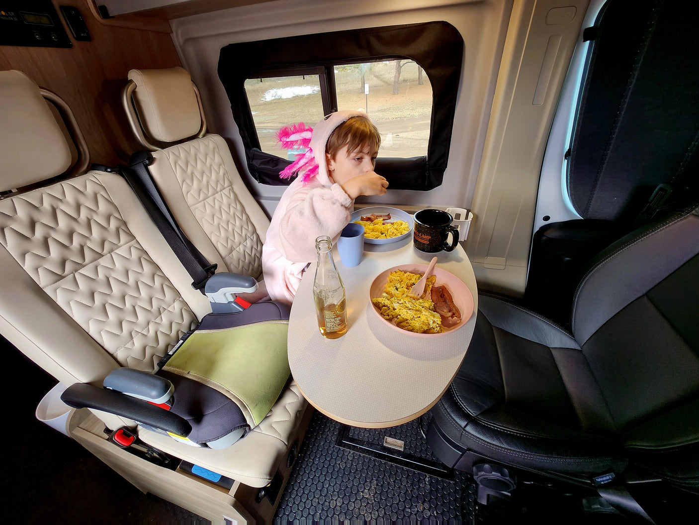 Child in a pink axolotl robe eats breakfast at a table in an RV rental, a cozy scene for family travels.