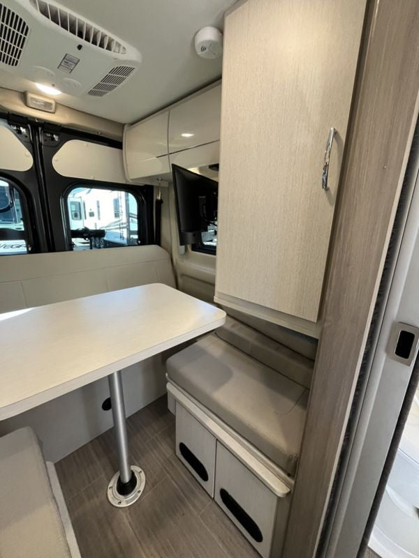 RV rental interior: light wood dinette with bench seating, overhead storage, and ceiling AC unit. Cozy and functional.