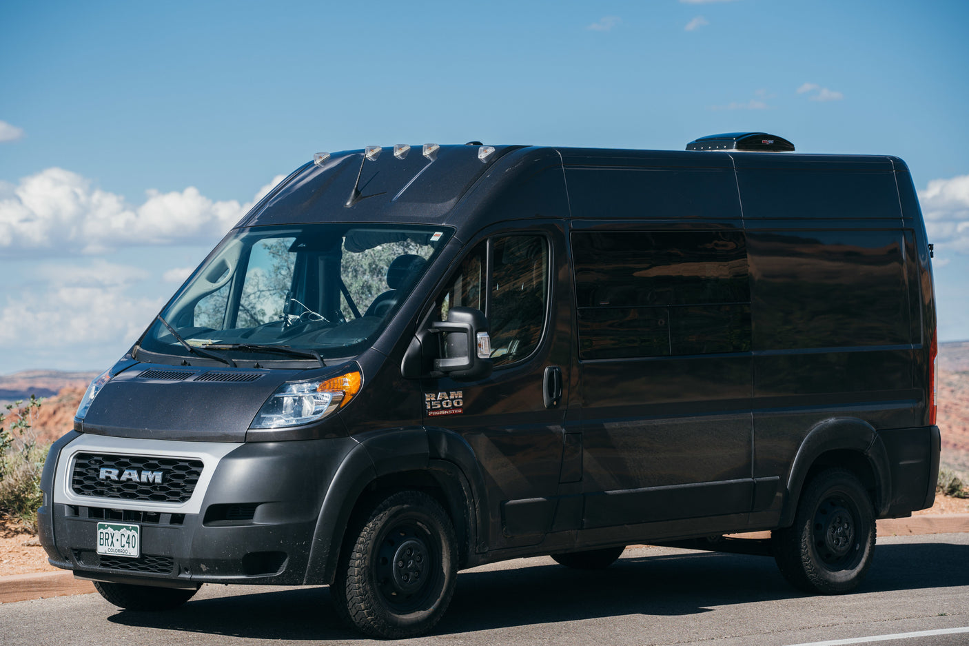 Dark gray Ram ProMaster camper van, an RV rental, parked in a scenic desert. Colorado plate BRX-C40.