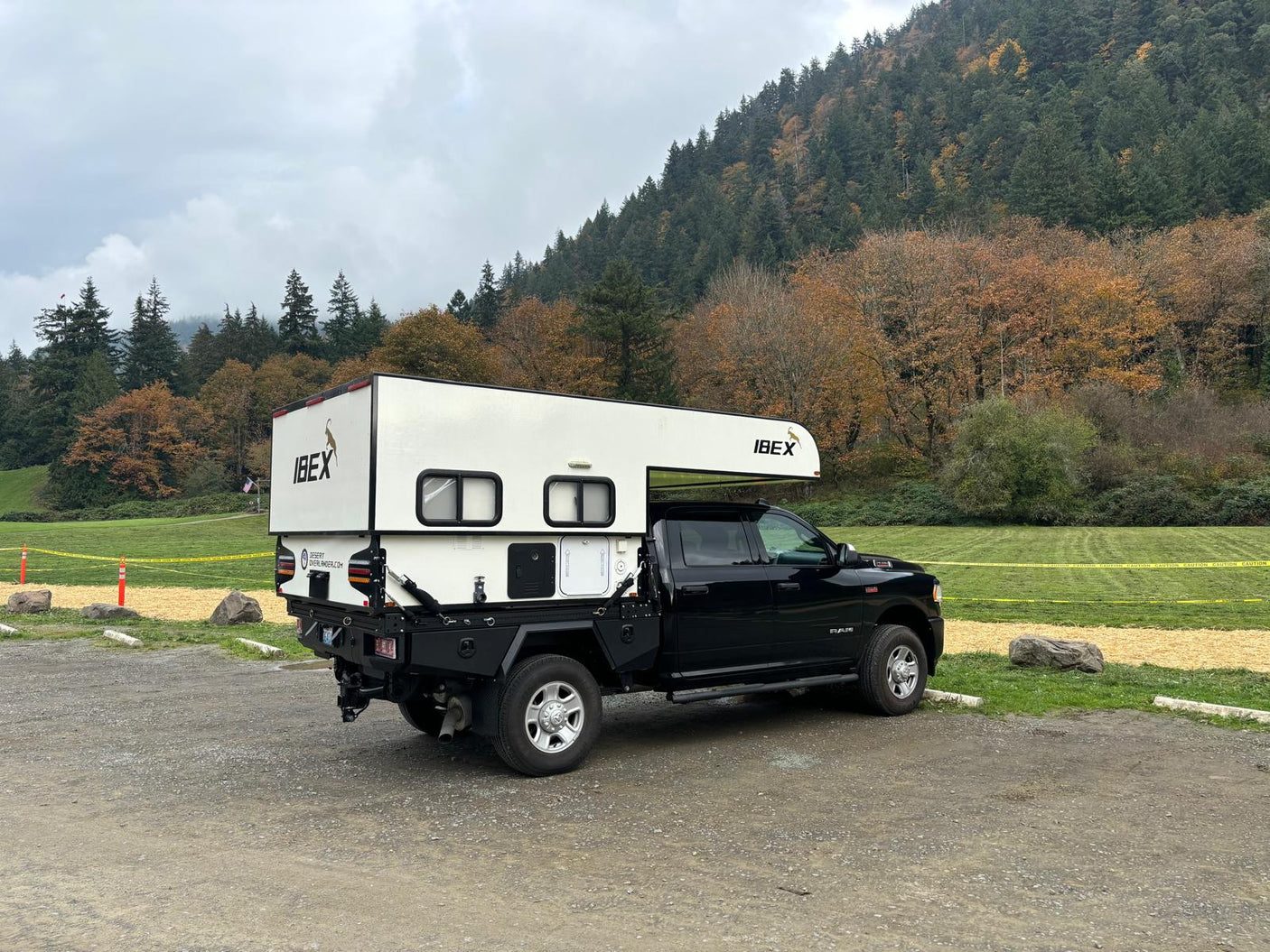 Black Ram truck with white IBEX truck camper parked by mountains. Ideal RV rental for exploring rugged landscapes.|Compact RV rental wet bath with wall-mount toilet & shower.|This RV rental offers a comfortable sleeping space with a wide bed
