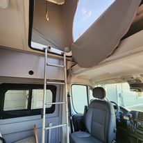 Explore this RV rental's cozy interior, featuring a ladder to the elevated pop-top bed and front cab area.