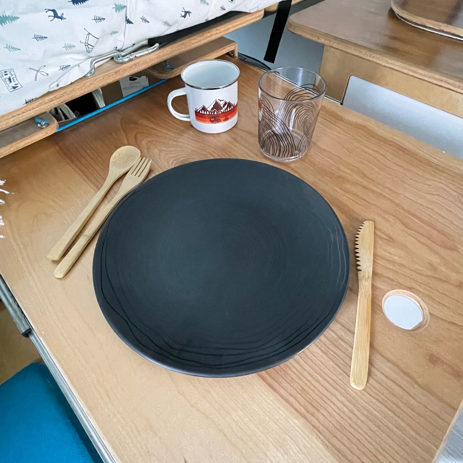 Enjoying a minimalist meal setup in an RV rental. Plate, bamboo utensils, mug, and patterned glass on a wooden table.