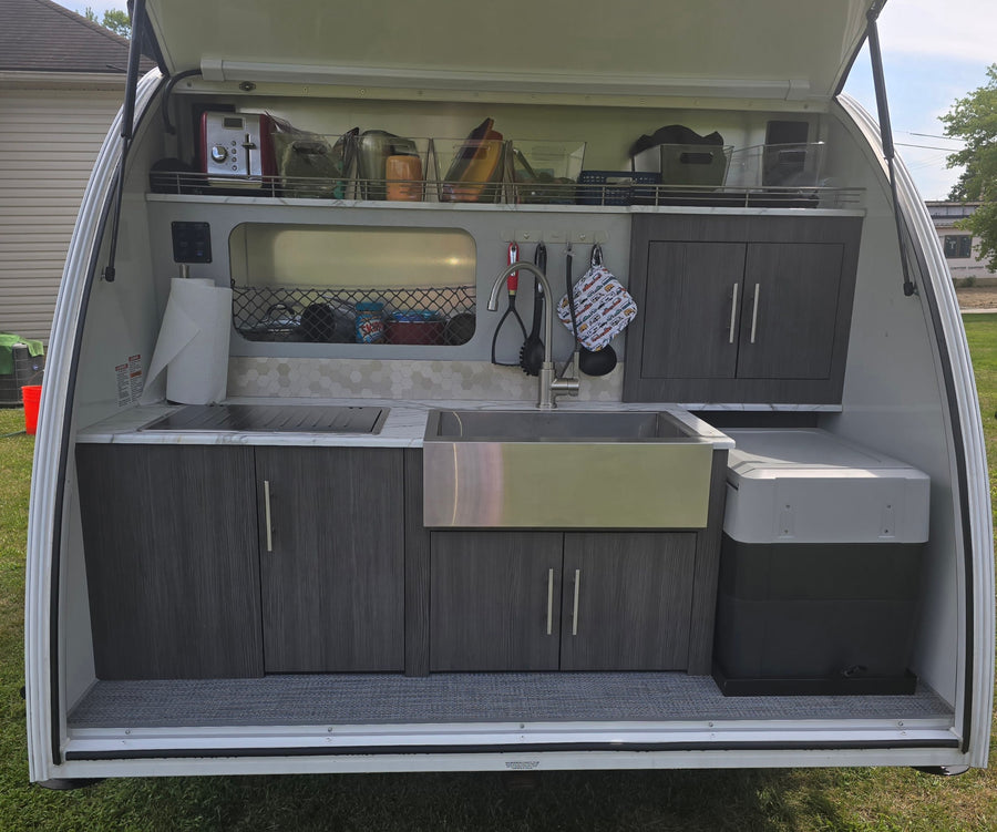 Explore this compact outdoor kitchen in an RV rental, featuring a sink, cooktop, and organized storage for easy camping meals.