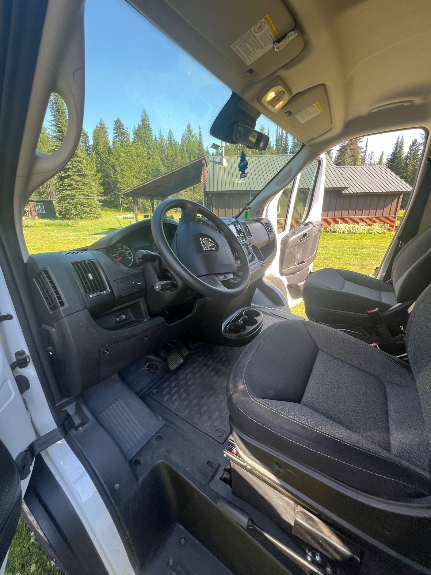 Step into this RV rental van! Interior view showing dashboard, driver's seat, and outside view of trees & buildings.