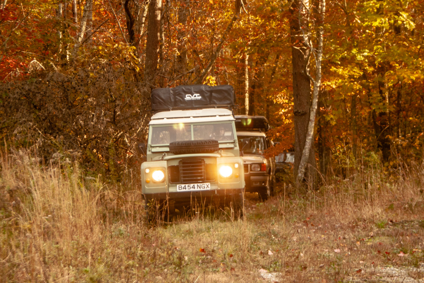 Two Land Rovers with rooftop tents navigate a vibrant fall forest trail, offering an adventurous alternative to RV rental for nature explorations.