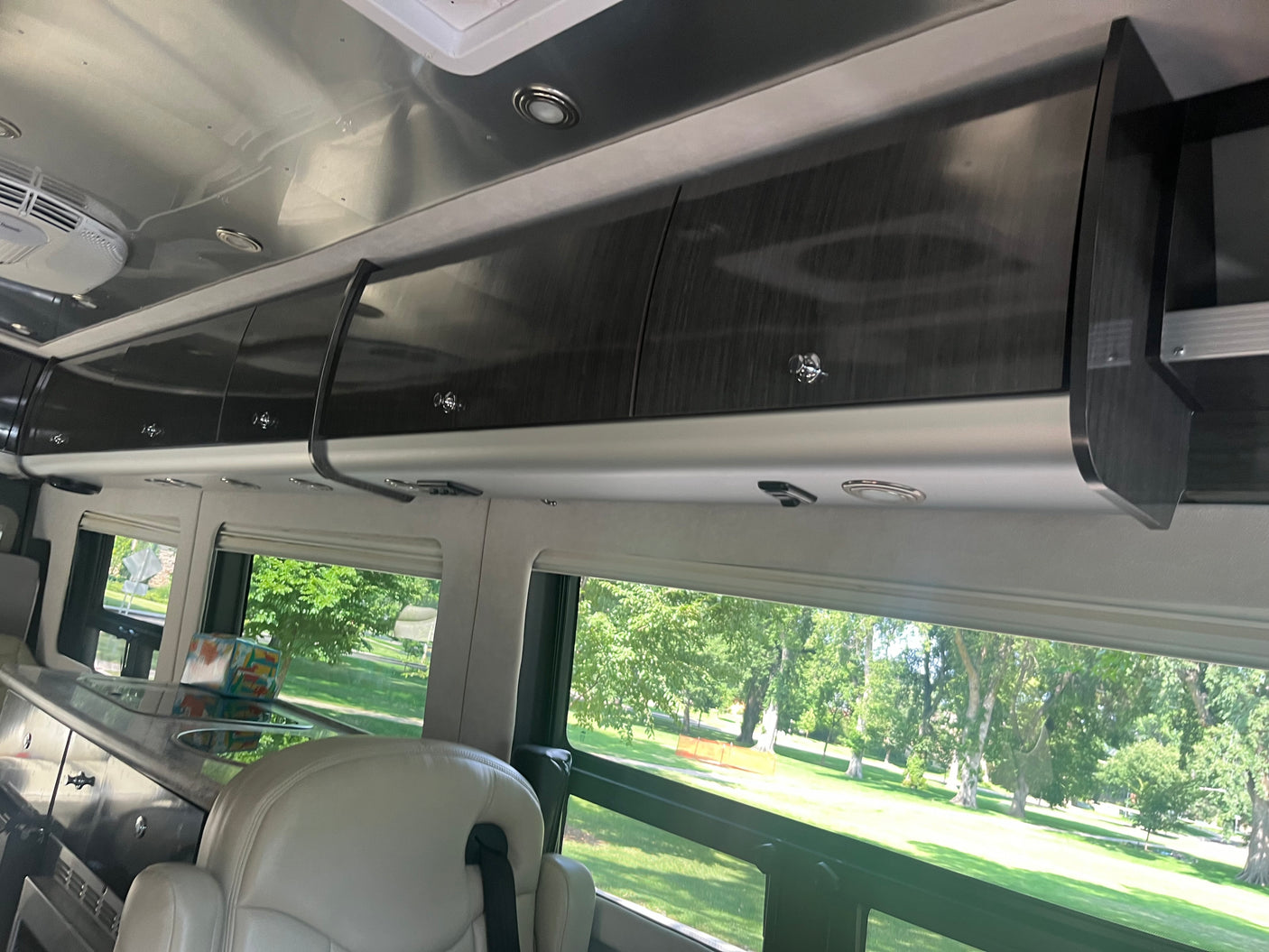 Inside a luxurious RV rental with sleek overhead cabinets, reflective ceiling, comfy seating, and expansive window views.