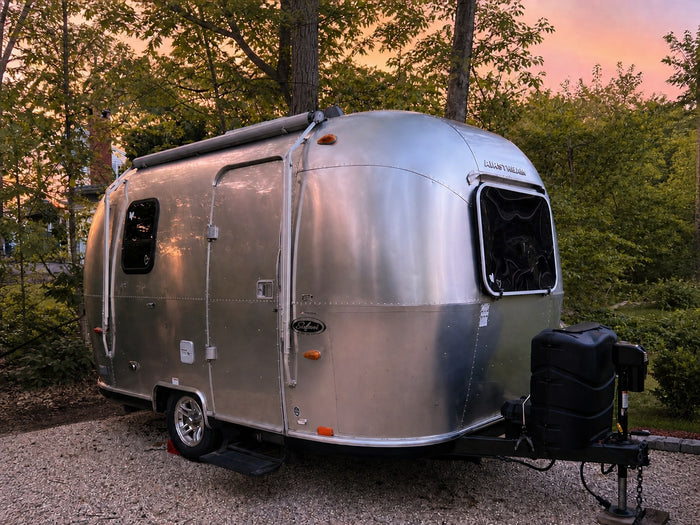 parked on a driveway near trees. Ready for adventure!|A silver Airstream RV rental glows under a colorful sunset