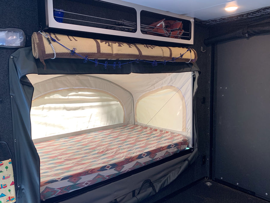 RV rental interior: a pop-up bunk bed with patterned mattress, overhead storage, and a rolled mat, ready for camping adventures.