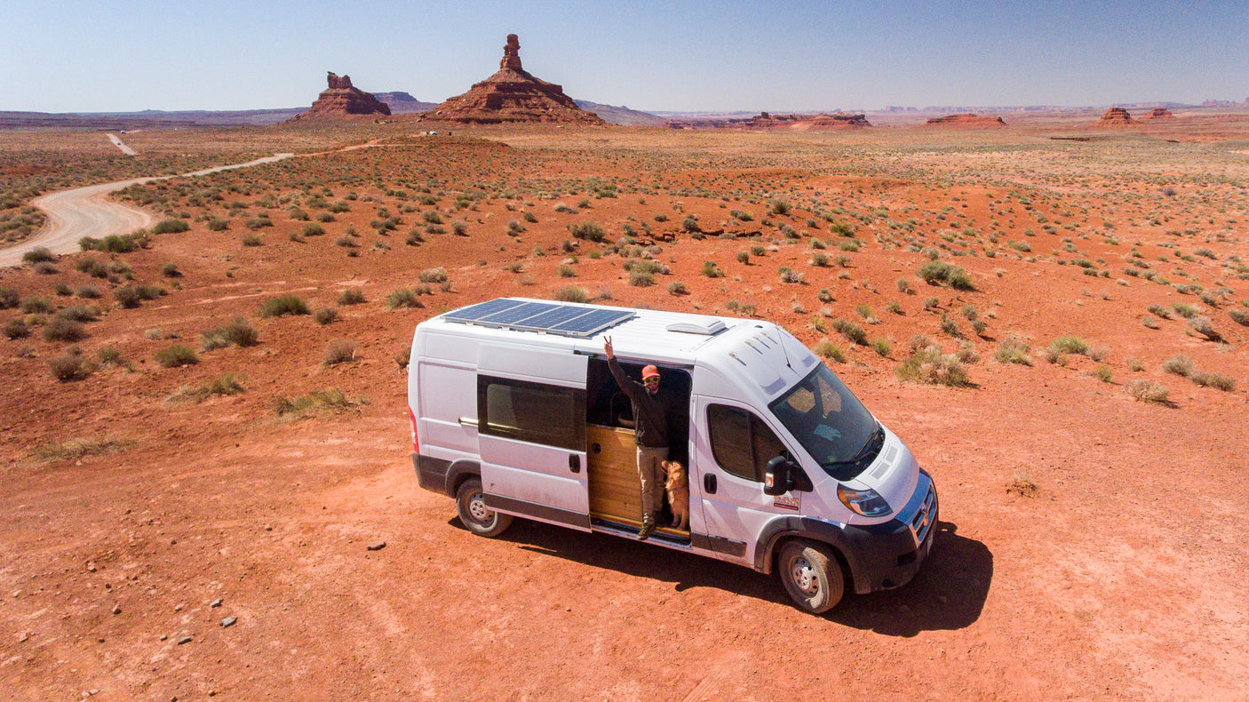 RV rental camper van with solar panels, man & dog in a vast red desert landscape.