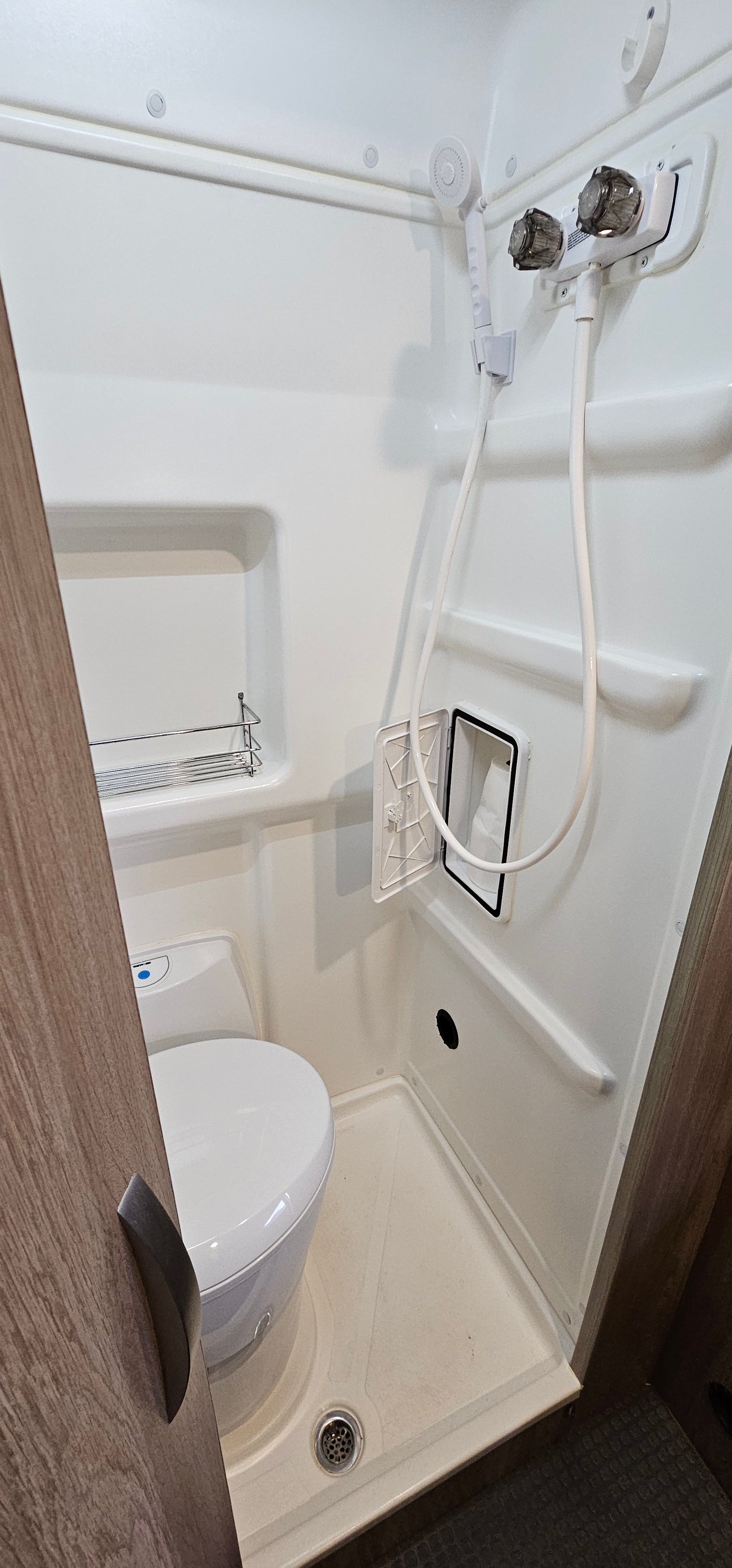 Inside an RV rental: a compact white wet bath featuring a toilet, handheld shower, and recessed storage, designed for efficiency.