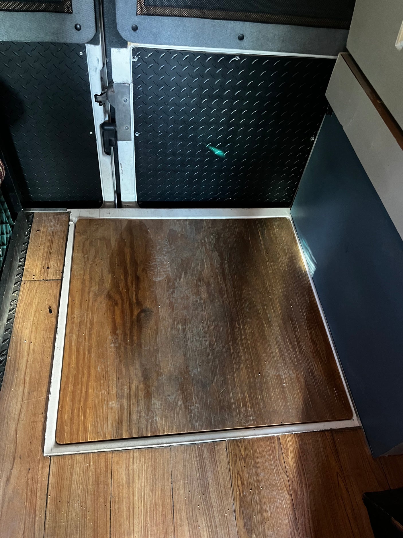 RV rental interior: wooden floor with a removable access panel, diamond plate door, and dark blue cabinet.