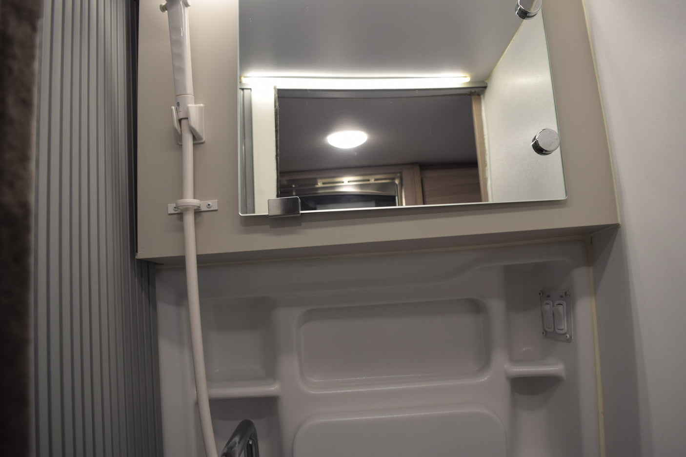 RV rental bathroom: A clean, compact space with a shower, mirror reflecting the RV interior, and light/fan controls.