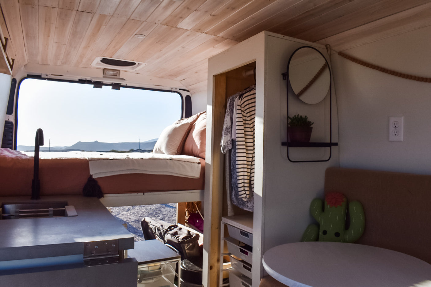 Cozy RV rental interior: kitchen sink, elevated bed, wardrobe, and dinette with a scenic mountain view.
