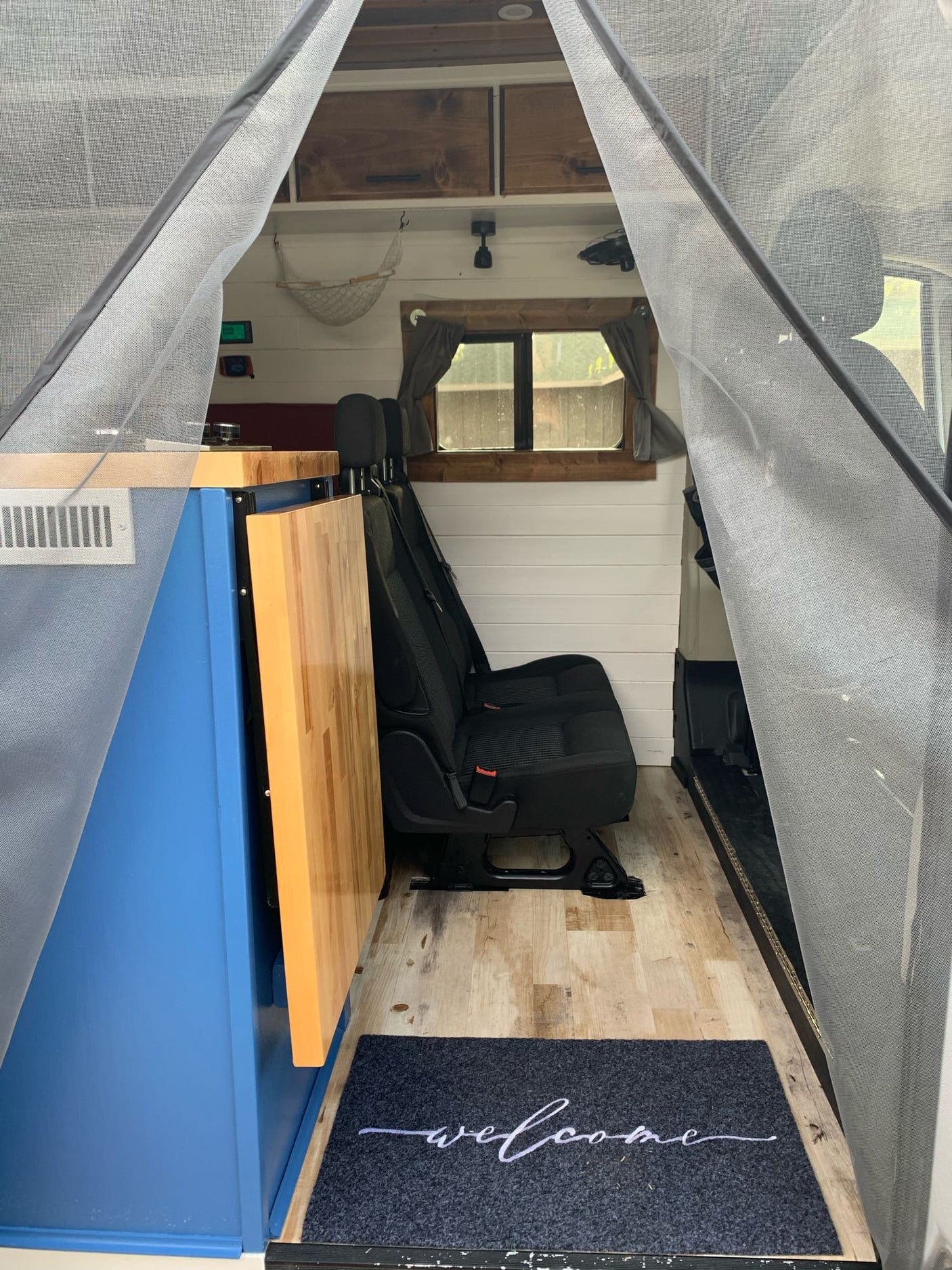 Step into this rv rental's comfy interior! Features a blue counter, fold-out table, passenger seats, and mesh door.