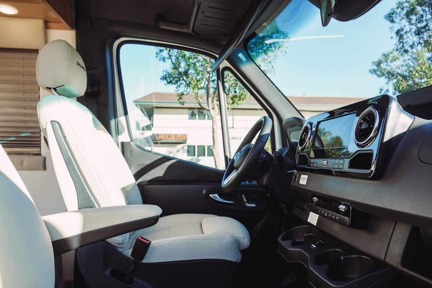 Luxury RV rental interior with bright driver's seat, Mercedes-Benz dashboard, and sunlit outdoor view. — photo 7