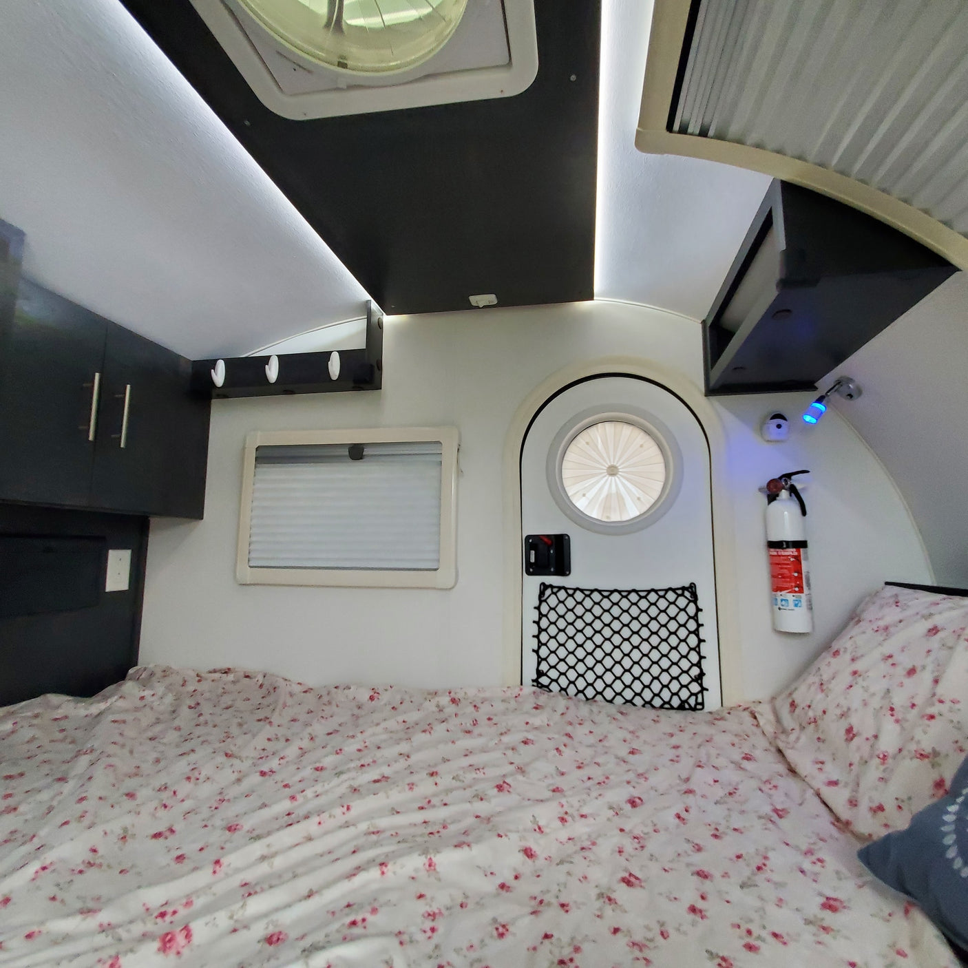 RV rental bedroom view: Floral bed, cabinets, and a unique round window create a cozy camper interior.