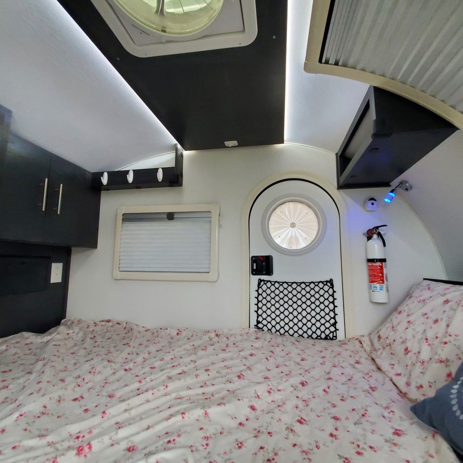 RV rental bedroom view: Floral bed, cabinets, and a unique round window create a cozy camper interior.