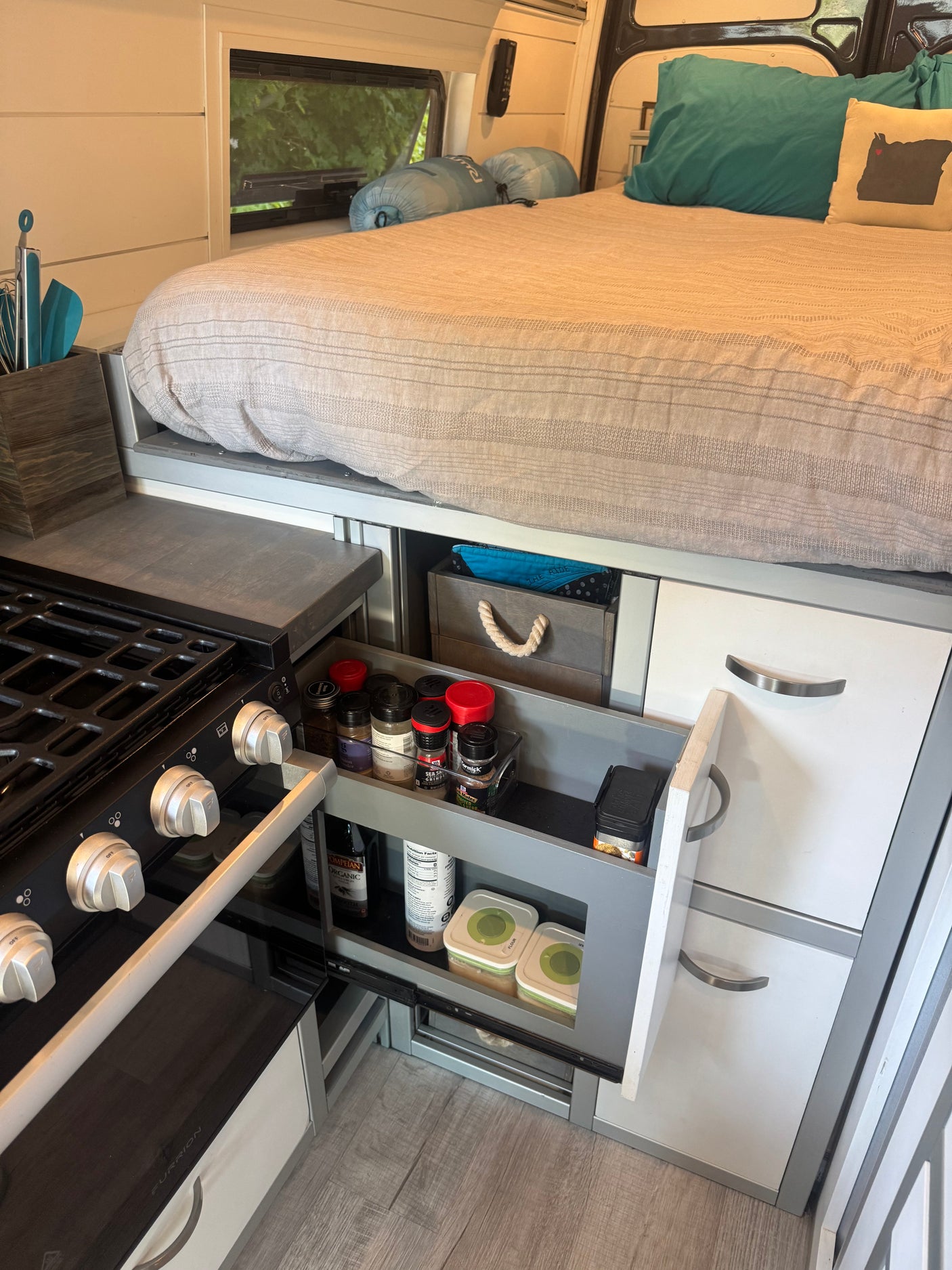 Cozy RV rental interior showcasing a compact kitchen, elevated bed, and efficient pull-out storage drawers.