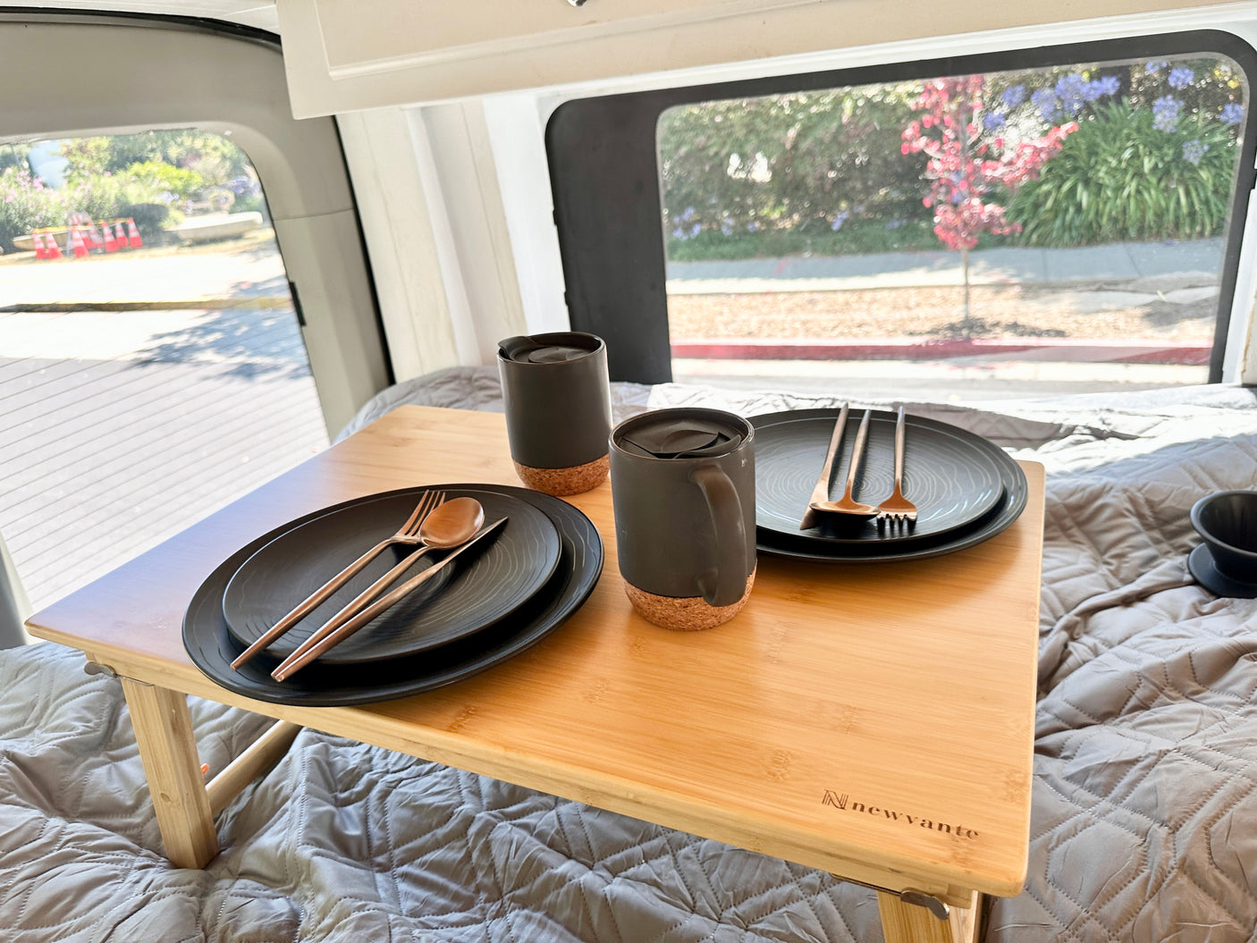 Cozy rv rental interior with a bed, lap desk, and complete dining set for two, offering a view of nature.