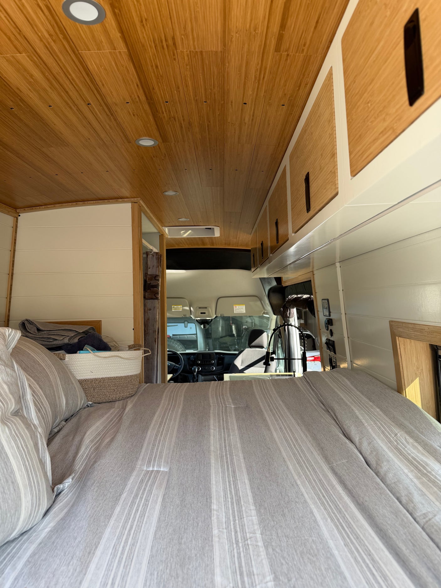 Cozy RV rental interior with a striped bed, wood ceiling, and a clear view to the driver's cabin in a camper van.