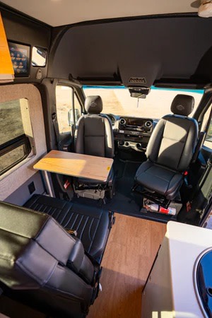 RV rental interior: Front cockpit with swivel seats, a removable dining table, rear bench, and kitchenette counter.