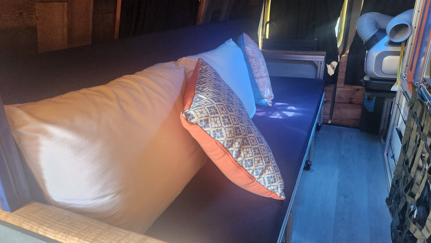 Cozy rv rental interior: dark blue bed with comfy pillows, wooden trim, and a portable AC unit.