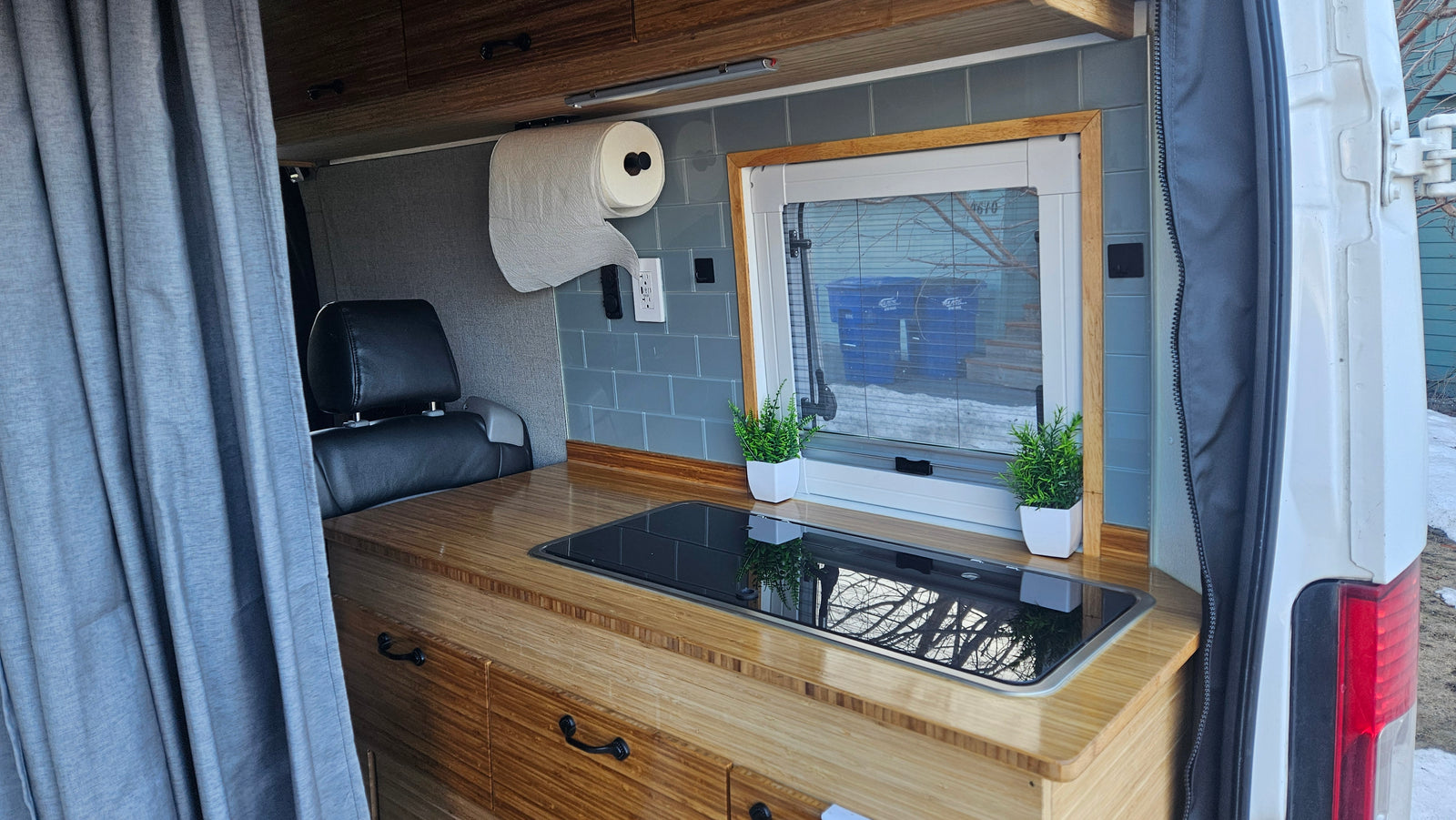 Compact RV rental interior featuring a bamboo kitchen counter with cooktop, window, and storage.